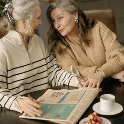 Two women drinking coffee while working on a crossword puzzle